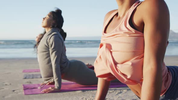 Group of diverse female friends practicing yoga, stretching at the beach