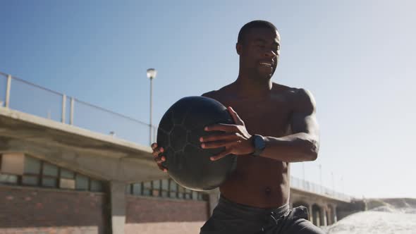 Focused african american man lifting ball, exercising outdoors on beach