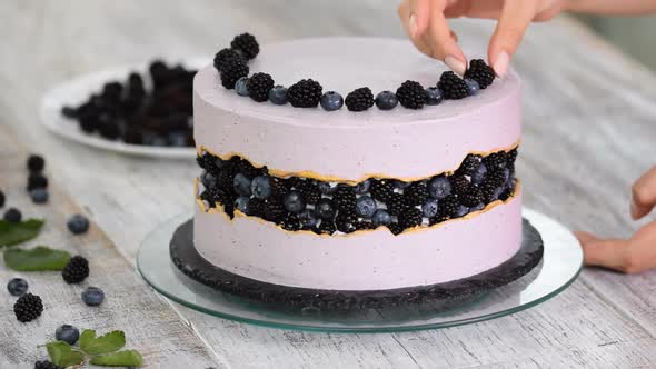 Confectioner decorates a beautiful cake with blueberries and blackberries.	