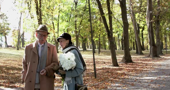 Elegant Elderly Couple with Bouquet of Flowers Talking with Gestures in Park