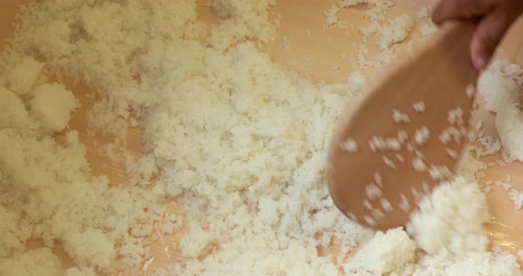 Chef's Hand Mixing Japanese Sushi Rice Using A Wooden Spoon Into A Traditional Wooden Sushi Bowl. -