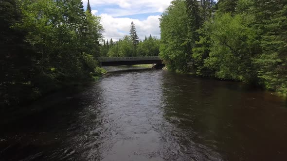 aerial fly over river towards bridge in wilderness 4k