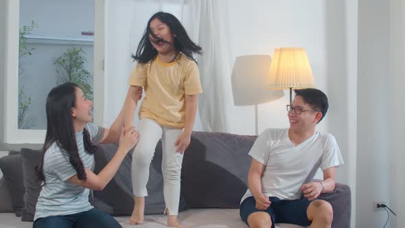 Happy young Asian family listen to music and dancing on sofa at home.