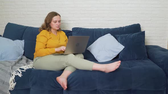 Woman is Sitting on the Sofa with Laptop and Typing Something