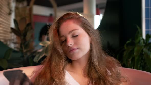 Pretty Girl With Long Hair In White Men's Shirt Sits In The Bathtub In The Bathroom.