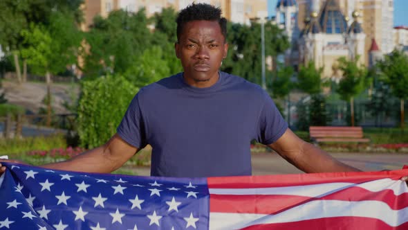 Camera Zoom in Patriot AfroAmerican Man Holding American Flag and Looks Camera