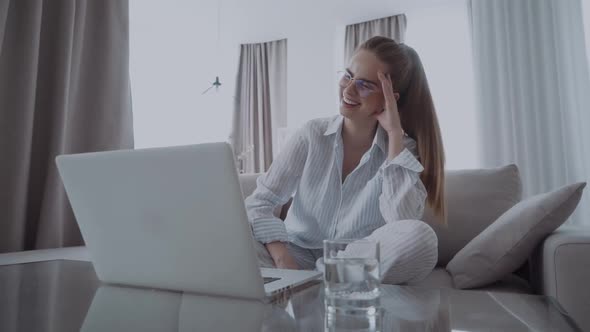 Happy Smiling Woman Sitting on Sofa and Using Laptop at Home, Looking at Screen and Laughs, Watching