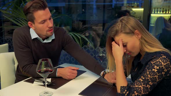 A Man and a Woman Sit at a Table in a Restaurant, the Woman Is Sad, the Man Tries To Comfort Her