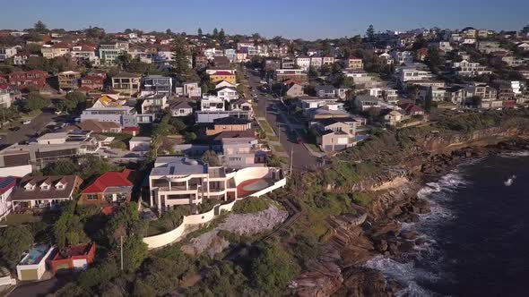 Beautiful reverse drone shot of houses near the beach and cliff with view of pacific ocean waves cra