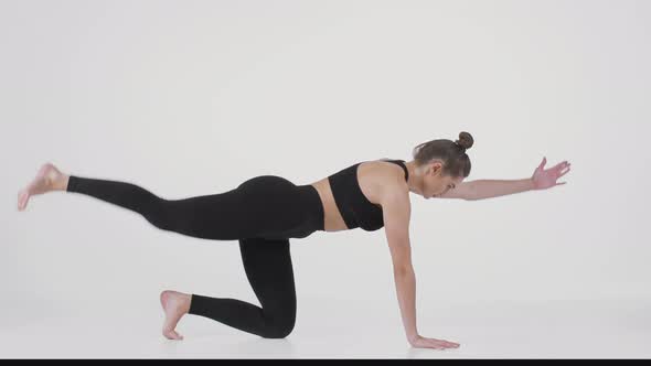 Young Sporty Woman Kneeling on Floor and Practicing Back Stretching Pose Raising Leg and Hand and