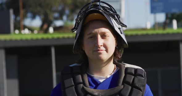 Portrait of caucasian female baseball player, catcher, in protective clothing, smiling on field