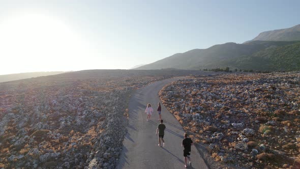 Friends travel concept. Four young tourists walking along empty rocky rural road in the countryside.