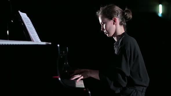 A young woman calmly plays the piano in the spotlight on the stage