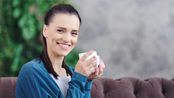 Medium Closeup Portrait of Smiling Domestic Woman Holding White Mug and Looking at Camera