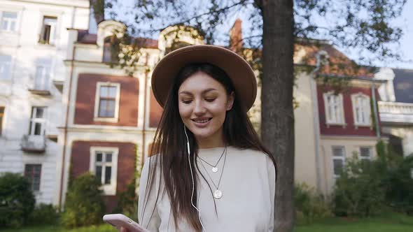 Young Woman in Lovely Hat Walking Near Beautiful House and Listening Music