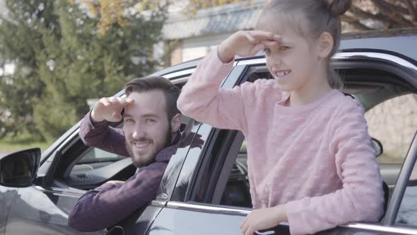 Portrait Little Girl on the Back Seat of the Car Leaned Out of the Window Close Up. The Father Is on