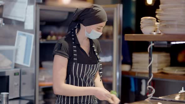 Young Female Cook in Apron and Covid19 Face Mask Preparing Ingredients for Fridge in Restaurant