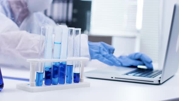 Close Up of Scientist Typing on Her Laptop and Smoking Blue Fluid in Test Tubes