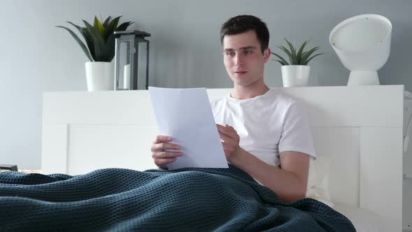 Man Excited After Reading Documents in Bed