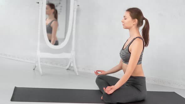 Yoga Woman Breathing Sitting in Lotus Position Relaxing on Mat at White Room