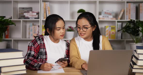 Twin asian girls using laptop and smartphone to learning online