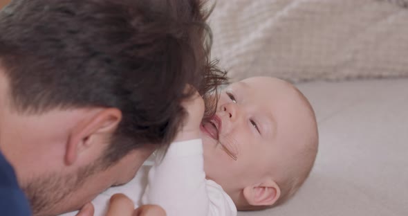 Close Up of the Head of Bearded and Mustashed Father Who is Kneeling By the Baby Lying on the Couch