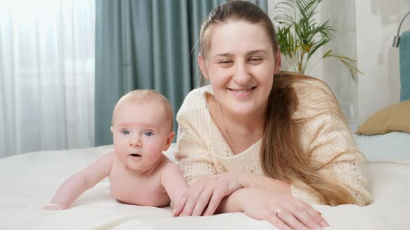 Adorable Baby Boy with Mother Lying in Bed and Smiling at Camera