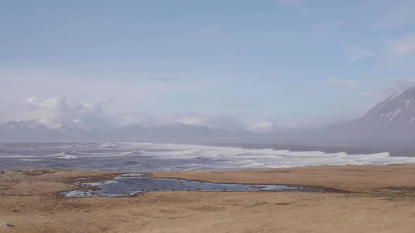 Iceland, view of ocean waves and mountains with snow from Hvalnes lighthouse