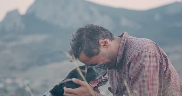 A Man Hugs His Spotted Dog Against the Backdrop of a Mountain Landscape