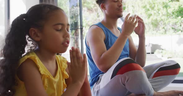 Happy biracial father and daughter doing yoga, meditating together