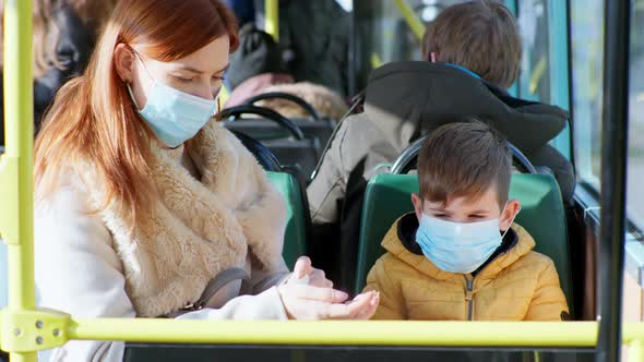 Female Parent Wearing Medical Mask with Their Male Child Treats Hands with Antiseptic To Protect