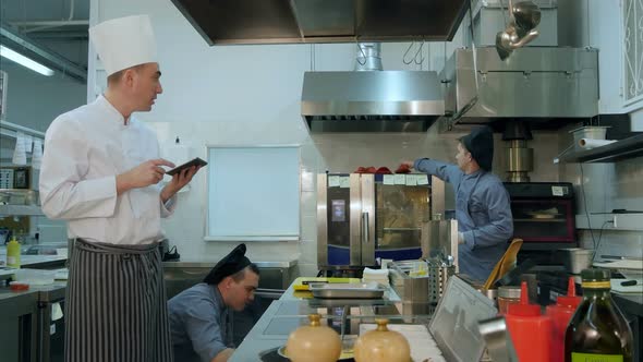 Chef Holding Tablet Discussing Something with Young Trainee