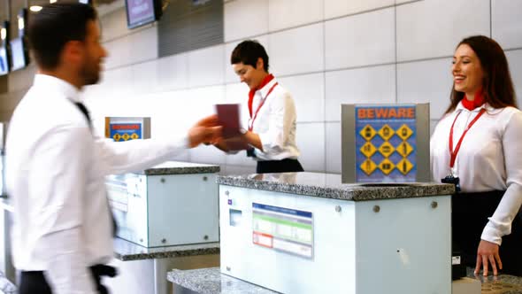 Two female airport staff checking passport and interacting with commuters at check-in desk