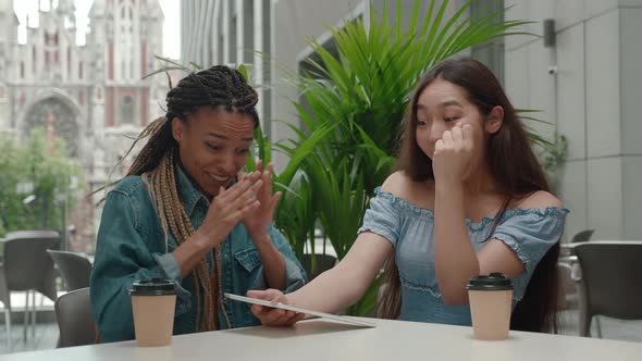 Two Multiracial Teenage Girls Sitting in Cafe and Using Tablet Computer