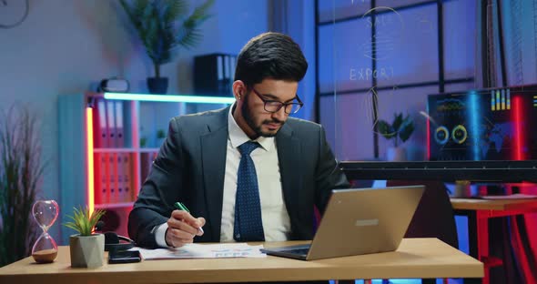 Businessman in Suit Working with Computer and Papers when Staying in the Evening in Office
