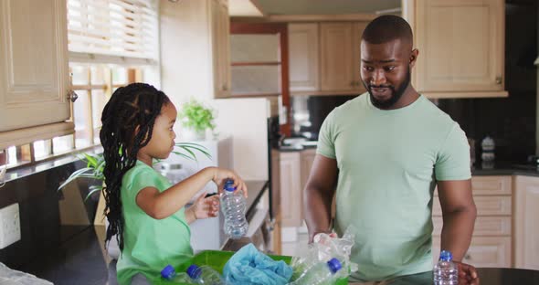 Happy african american father and daughter sorting recycling and crushing plastic bottles in kitchen