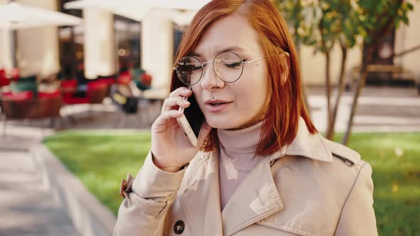 Young Woman is Talking on Cellphone While Standing Nearby an Openair City Cafe