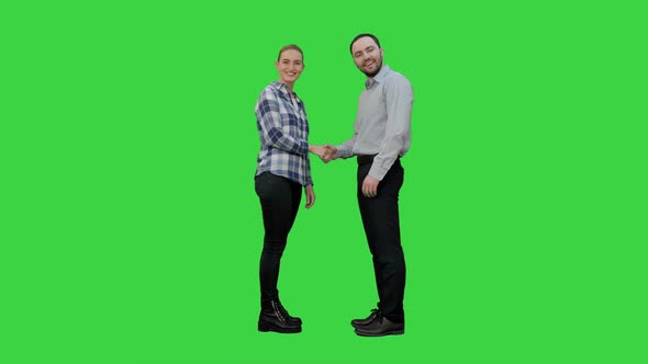 Two Young People in Casual Shake Hands, Look at Camera and Thumb Up on a Green Screen, Chroma Key