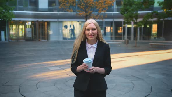Formal Young Lady Drinking Coffee in Patio. Elegant Blond Woman in Suit and with Long Hair Drinking