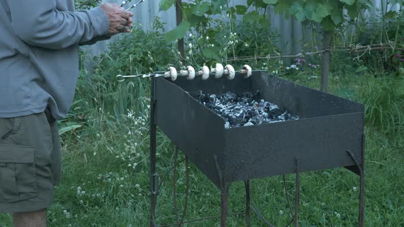 Skewers of mushrooms. Grilled mushrooms. Man puts skewers of vegetables on brazier