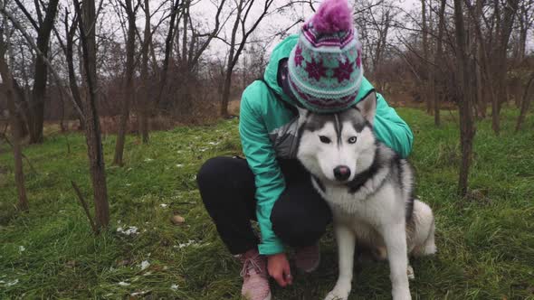 Young Beautiful Woman Walks and Plays with Her Husky Dog at Winter Around Forest