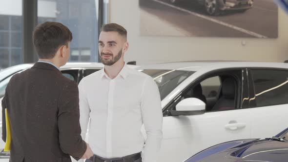 Happy Young Man Receiving Car Keys to His New Auto From the Salesman