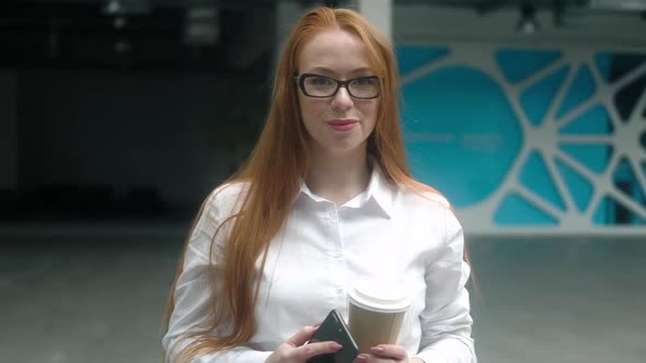 Portrait businesswoman in lobby of business building with a phone and coffee