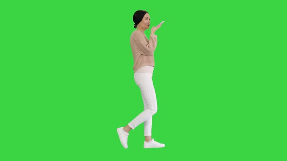 Young Woman Talking on the Phone Holding It To Her Face While Walking on a Green Screen, Chroma Key.
