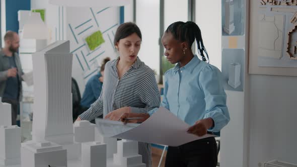 Workmates Analyzing Blueprints Plan and Building Model on Table Working on Construction