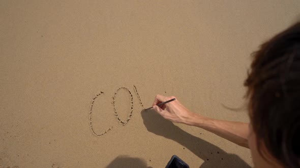 Slowmotion Shot. A Man Writes Lettering COVID-19 on the Sand on a Beach