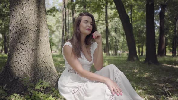 Portrait of Glamorous Young Girl with Long Brunette Hair Wearing a Long White Summer Fashion Dress