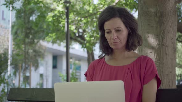 Thoughtful Middle Aged Woman Using Laptop in Summer Park