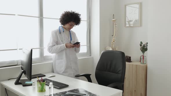 Young Woman Doctor Using Her Mobile Phone in the Clinic