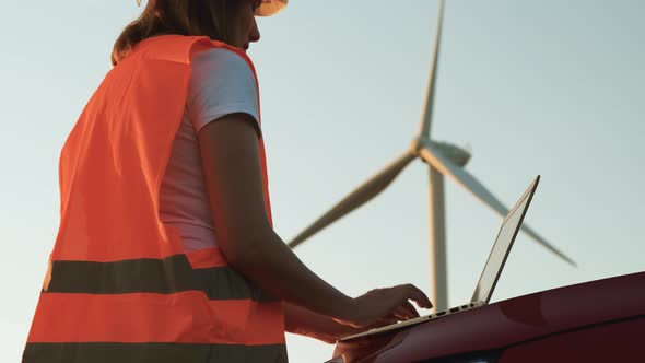 An Windmill Engineer Supervises the Work of the Wind Turbines on the Laptop Standing Near the Car